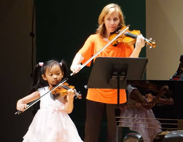 Young violin student performing with teacher on stage